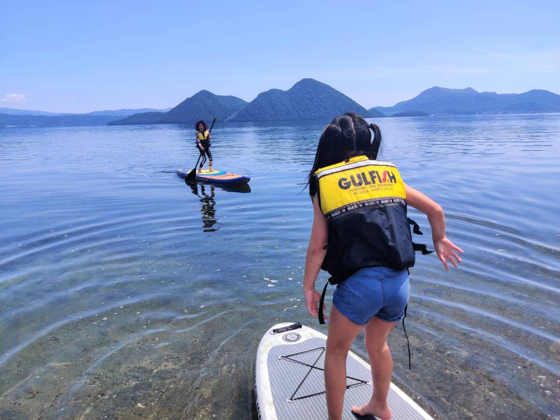 Children stand-up paddle boarding on the lake in summer in Niseko region